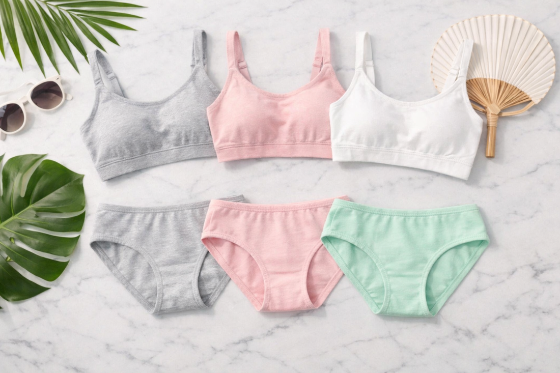 Flat lay of cotton bras and panties in grey, pink, white and mint green on a marble surface with tropical leaves, sunglasses and a fan — best summer lingerie for Indian women 2026